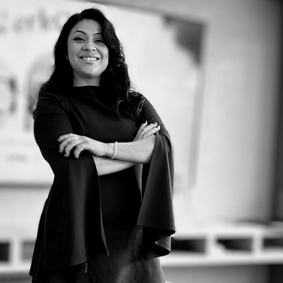 Black and white portrait of Roxy Castrejon standing with her arms crossed, smiling.