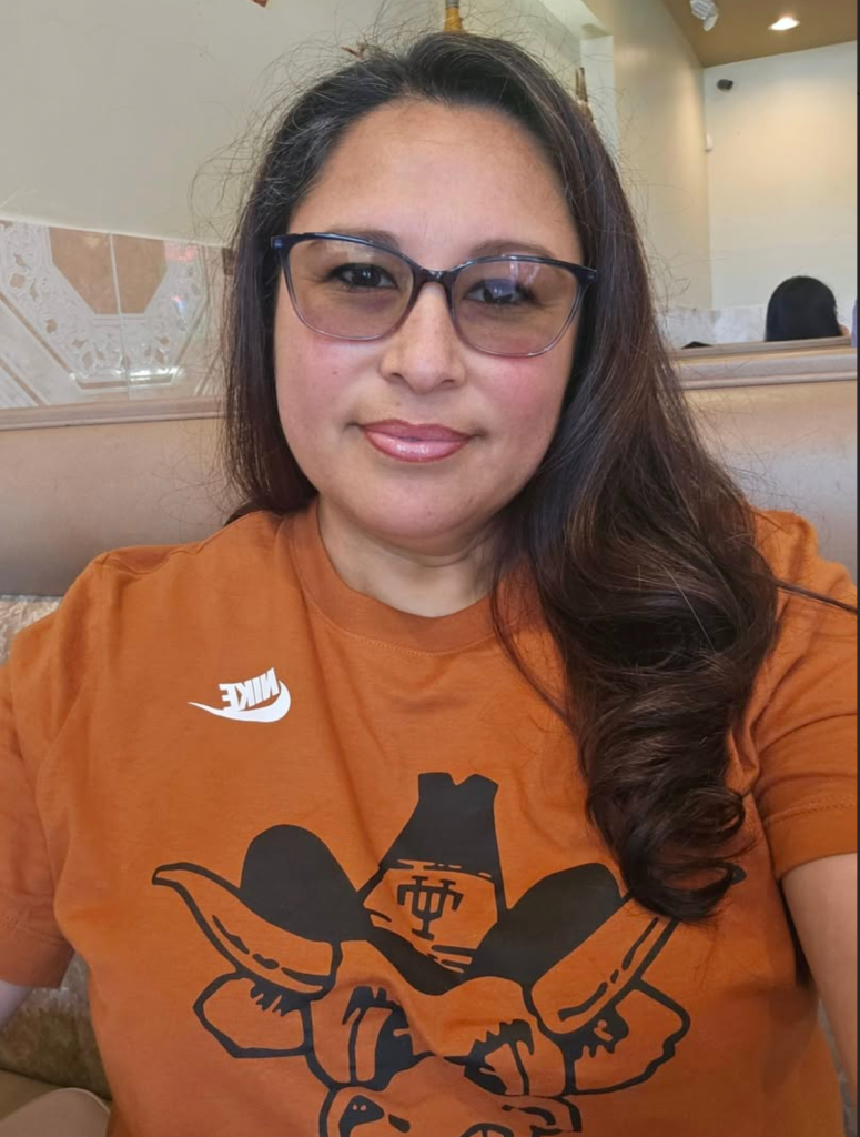 Portrait of Veronica Castillo smiling, wearing glasses and an orange shirt.
